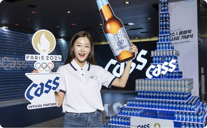주류 브랜드 최초 논알코올 음료 올림픽 공식 글로벌 파트너 지정되어 cass0.0 병맥주를 여성이 들고있습니다.