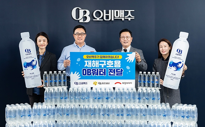오비맥주 임직원이 ‘재해구호용 OB워터 전달’ 문구가 적힌 현수막을 들고 구호용 생수 박스와 함께 기념촬영하는 모습이 있습니다